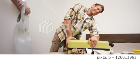 Image of young man, tourist struggling to close his suitcase full of clothes, pushing on bag, trying to press items inside luggage to shut the zipper, packing for travelling abroad, going on holiday 126013963