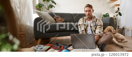 Man with laptop on suitcase, sits with dog on floor, looks online, browsing websites, packs clothes for vacation, goes on holiday, plans trip abroad Man with laptop on suitcase, sits with dog on floor, looks online, browsing websites, packs clothes for vacation, goes on holiday, plans trip abroad 126013972