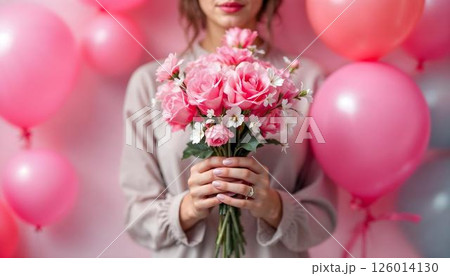 A woman proudly displays a bouquet of pink rose on a pink backdrop, symbolizing strength on International Women's Day 126014130