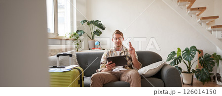 Man makes a wish, looks at digital tablet, has suitcase packed and ready for holiday, goes on vacation, picks tour on travel agency website Man makes a wish, looks at digital tablet, has suitcase packed and ready for holiday, goes on vacation, picks tour on travel agency website 126014150