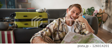 Portrait of handsome smiling young man, tourist shows call me gesture, phone hand, holding travel map, inviting to go on holiday, packed suitcase Portrait of handsome smiling young man, tourist shows call me gesture, phone hand, holding travel map, inviting to go on holiday, packed suitcase 126014201