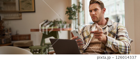Portrait of man with serious face, sitting in cafe with laptop and smartphone, pointing at you with warning, scolding you, frowning with disapproval Portrait of man with serious face, sitting in cafe with laptop and smartphone, pointing at you with warning, scolding you, frowning with disapproval 126014337