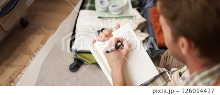 Close up portrait of man packing suitcase, making notes, check-list of items he wants to take on holiday, packing luggage Close up portrait of man packing suitcase, making notes, check-list of items he wants to take on holiday, packing luggage 126014417