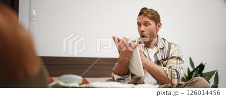 Portrait of tourist checking his notes, making list of items for holiday, writing down ideas, packing suitcase, sitting on bed, getting ready for vacation 126014456