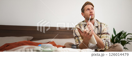 Portrait of thoughtful young man, tourist going on vacation, going through holiday check-list, writing down what he wants to take on travelling 126014479
