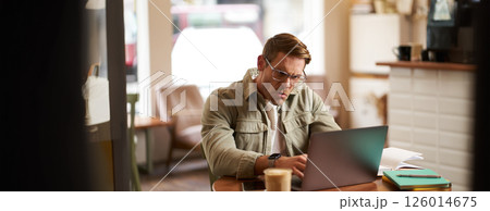 Portrait of angry man in glasses, looking frustrated and typing something on laptop, staring at screen with outraged face expression, sitting in cafe Portrait of angry man in glasses, looking frustrated and typing something on laptop, staring at screen with outraged face expression, sitting in cafe 126014675