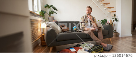 Portrait of young man packing for a trip, going on vacation, putting clothes inside suitcase, preparing for holiday Portrait of young man packing for a trip, going on vacation, putting clothes inside suitcase, preparing for holiday 126014676
