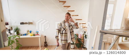 Portrait of handsome young man going on a trip, shows mobile phone hand sign gesture, going on vacation, leaving the apartment with suitcase, carrying luggage in hand Portrait of handsome young man going on a trip, shows mobile phone hand sign gesture, going on vacation, leaving the apartment with suitcase, carrying luggage in hand 126014800