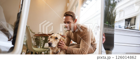 Close up portrait of handsome man with his dog, sitting in cafe. A guy drinks his coffee and touches golden retriever Close up portrait of handsome man with his dog, sitting in cafe. A guy drinks his coffee and touches golden retriever 126014862