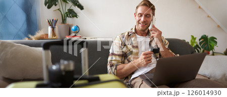 Image of guy calling someone, holding credit card and using laptop, has suitcase and camera packed for holiday 126014930