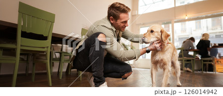 Close up portrait of handsome happy man petting his cute dog in a pet-friendly cafe. Coffee shop visitor with his golden retriever 126014942
