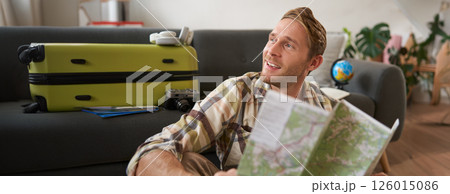 Handsome smiling tourist, man holds map, plans his holiday, going on vacation, looking aside with dreamy, happy face expression Handsome smiling tourist, man holds map, plans his holiday, going on vacation, looking aside with dreamy, happy face expression 126015086