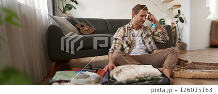 Portrait of guy in panic, packs suitcase, looks stressed and worried, clueless what to bring on holiday 126015163