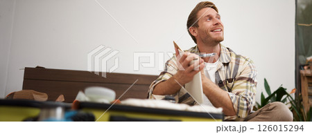 Close up portrait of smiling young man, writing down notes, holding pen and notebook, check-list of items in suitcase, going on holiday Close up portrait of smiling young man, writing down notes, holding pen and notebook, check-list of items in suitcase, going on holiday 126015294