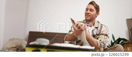 Portrait of thoughtful young man, tourist going on vacation, going through holiday check-list, writing down what he wants to take on travelling Portrait of thoughtful young man, tourist going on vacation, going through holiday check-list, writing down what he wants to take on travelling 126015299