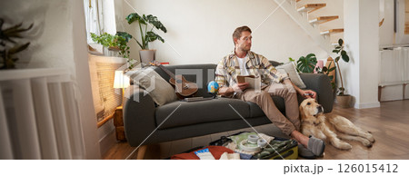 Portrait of man sitting with his dog, packing suitcase for a holiday, going on trip with a pet Portrait of man sitting with his dog, packing suitcase for a holiday, going on trip with a pet 126015412