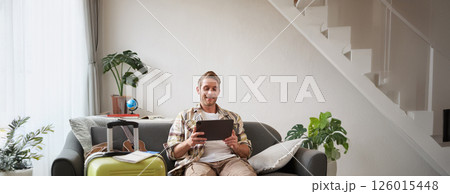 Vertical shot of man, tourist with suitcase, looking at digital tablet, reading about travel destination, booking hotel on gadget 126015448