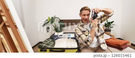 Portrait of handsome man going on vacation, packing suitcase, holding camera, travel photographer going on holiday Portrait of handsome man going on vacation, packing suitcase, holding camera, travel photographer going on holiday 126015461