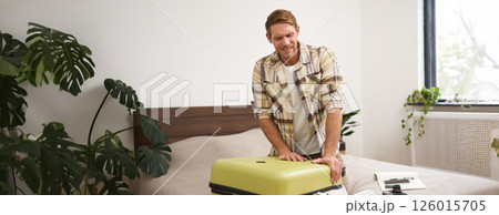 Image of young traveller, tourist struggling to shut his suitcase, pushing on luggage to close it, carry a lot of clothes on vacation Image of young traveller, tourist struggling to shut his suitcase, pushing on luggage to close it, carry a lot of clothes on vacation 126015705