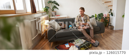 Portrait of young man packing for a trip, going on vacation, putting clothes inside suitcase, preparing for holiday Portrait of young man packing for a trip, going on vacation, putting clothes inside suitcase, preparing for holiday 126015770