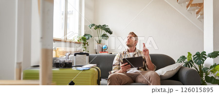 Portrait of tourist cross fingers, sits and waits with hope for good news, holds digital tablet, has suitcase and camera packed for holiday trip 126015895