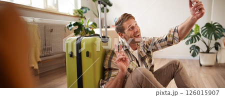 Portrait of smiling handsome man with suitcase, taking selfie with luggage, posting on social media about going on holiday Portrait of smiling handsome man with suitcase, taking selfie with luggage, posting on social media about going on holiday 126015907