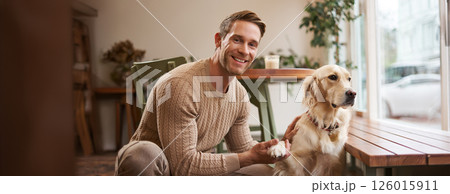 Portrait of young handsome dog-owner, spending time with his pet in a cafe, sitting indoors, looking outside window Portrait of young handsome dog-owner, spending time with his pet in a cafe, sitting indoors, looking outside window 126015911
