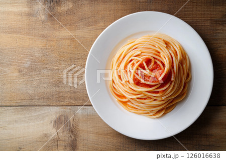 A plate of pasta topped with rich tomato sauce and fresh basil, served on a wooden table, showcasing a delightful and flavorful Italian meal. 126016638