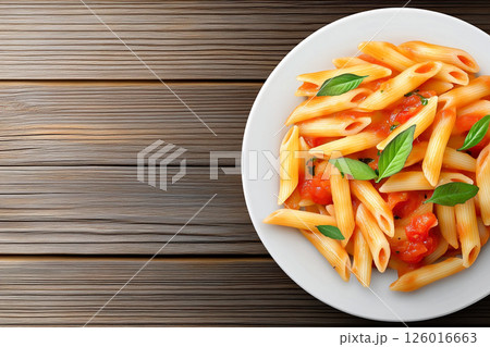 A plate of pasta topped with rich tomato sauce and fresh basil, served on a wooden table, showcasing a delightful and flavorful Italian meal. A plate of pasta topped with rich tomato sauce and fresh basil, served on a wooden table, showcasing a delightful and flavorful Italian meal. 126016663