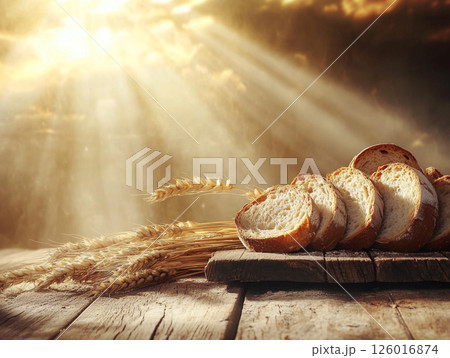 Freshly baked bread with a golden crust on a wooden surface, accompanied by wheat stalks and scattered grains, illuminated by warm glowing light. 126016874