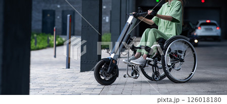 A faceless woman in a wheelchair with an assistive device for manual control. Electric handbike.  126018180