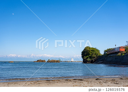 富山湾の雨晴海岸から残雪の立山連峰と上空にぽっかいりと浮かぶを背景に海岸線を走るJR氷見線の気動車 126019376
