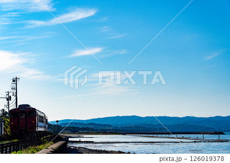 夕暮れ時の雨晴海岸を走るJR氷見線の気動車 126019378