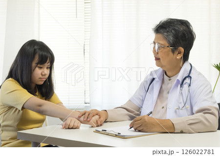 Asian girl and senior psychologist woman having therapy with digital tablet at clinic. 126022781