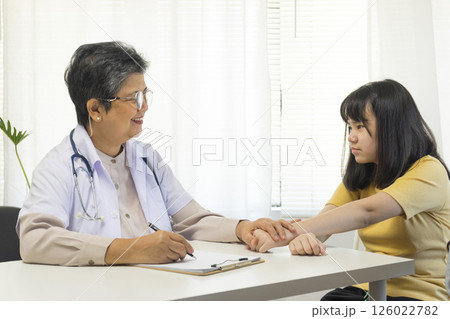 Asian girl and senior psychologist woman having therapy with digital tablet at clinic. 126022782