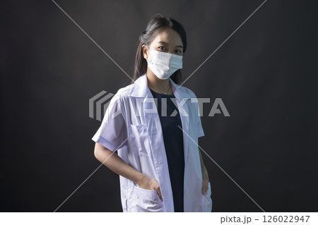 Young Asian female physician, Med student or resident doctors wear face mask standing on black background. 126022947