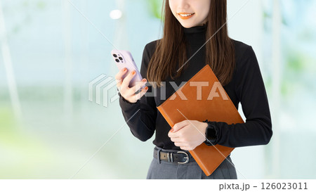 スマートフォンとバインダーを持つ笑顔の女性・ビジネスウーマン 126023011