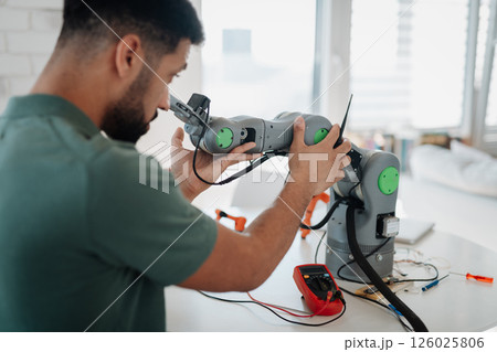 Young engineer building and programming a robotic arm at home. 126025806