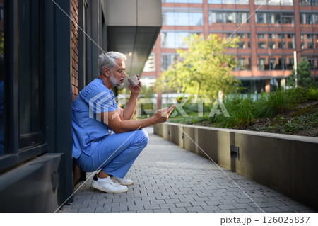 Healthcare worker outside hospital and checking phone during break. Healthcare worker outside hospital and checking phone during break. 126025837