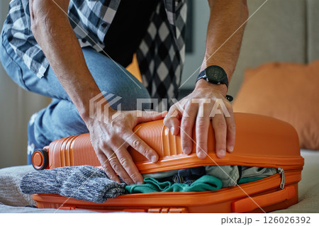 Man trying to close over packed suitcase before trip 126026392