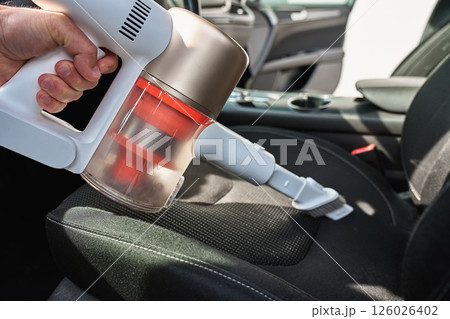 Man cleaning car dashboard with handheld vacuum cleaner 126026402
