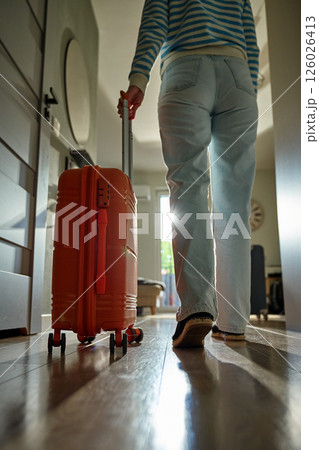 Woman rolls suitcase down hallway in apartment. Departure moment 126026413