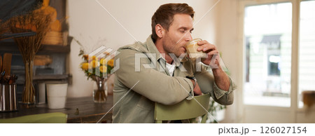 Portrait of handsome blond man in cafe, sits on chair, enjoys the taste of delicious freshly brewed cup of coffee Portrait of handsome blond man in cafe, sits on chair, enjoys the taste of delicious freshly brewed cup of coffee 126027154