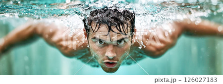 Male swimmer is performing a powerful stroke underwater, showcasing strength and determination while creating splashes in a vibrant aquatic environment 126027183