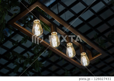 Four light bulbs are elegantly hanging down from a wooden frame 126027431