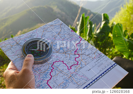 Traveler's hand holding directional tool on paper map during outdoor adventure 126028168