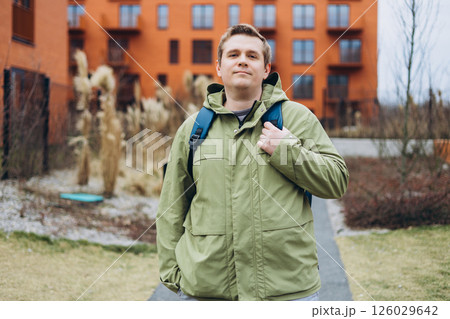 A handsome young man with backpack walking on the street in the city. Urban lifestyle concept. Traveler. Spring time. Portrait of happy young man in casual clothing standing outdoor. A handsome young man with backpack walking on the street in the city. Urban lifestyle concept. Traveler. Spring time. Portrait of happy young man in casual clothing standing outdoor. 126029642