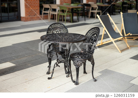 Wrought iron furniture dining table and chairs kept outside on a tiled floor at a cafe. 126031159