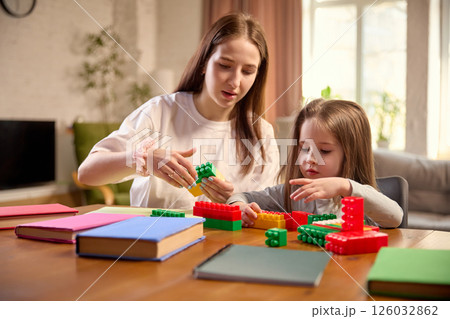 Mother and daughter engaged in shared building block activity, sitting at table in living room at home 126032862