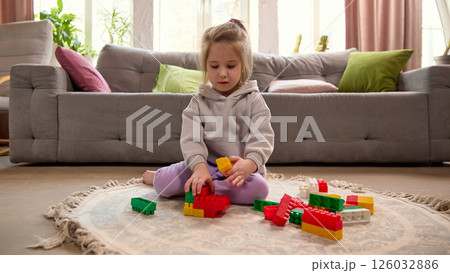 Young child sitting on carpet and involved in building with colorful blocks on floor. 126032886